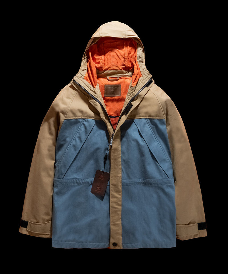 Left Hand Arctic Parka in tan and blue with orange lining, featuring a hood and zip closure, displayed against a black background.