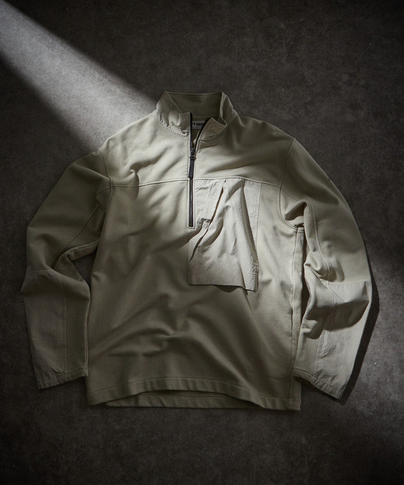 Left Hand Half Zip Sweat in light khaki with stand collar and chest pocket, laid flat under soft lighting on a dark surface.