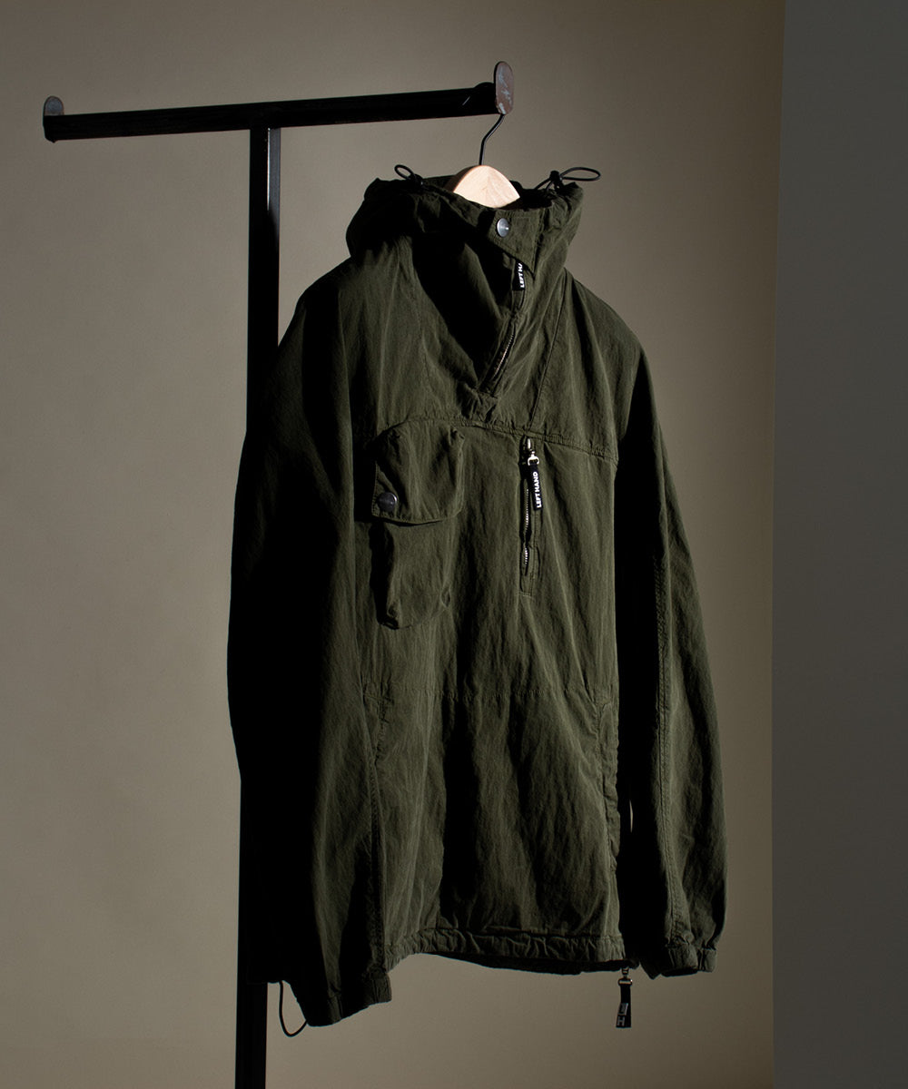 Left Hand Adda Smock in dark green with hood, zip detail and front pocket, displayed hanging on a rail against a neutral background.