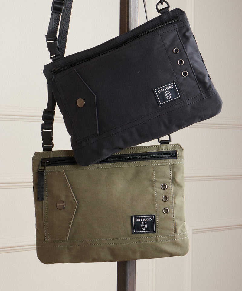Left Hand cross body bags in black and olive green with zip closures and metal details, displayed hanging indoors.