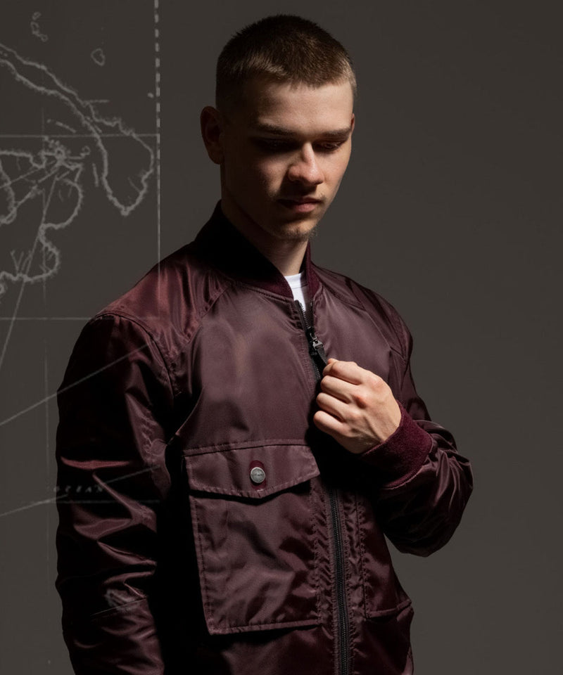 Left Hand Sateen Brembo Jacket in deep burgundy with zip fastening and flap pockets, worn by a model against a dark background.