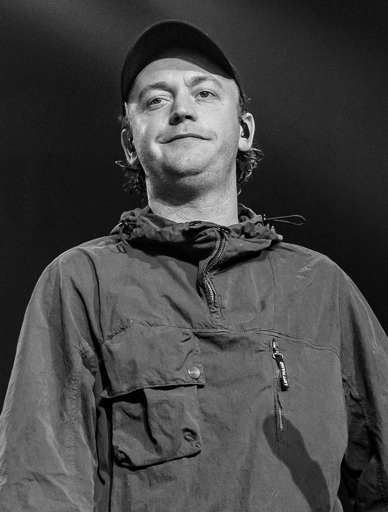 Tommy O'Dell, frontman of DMA’s, in a black and white portrait wearing a cap and jacket, looking ahead on stage.