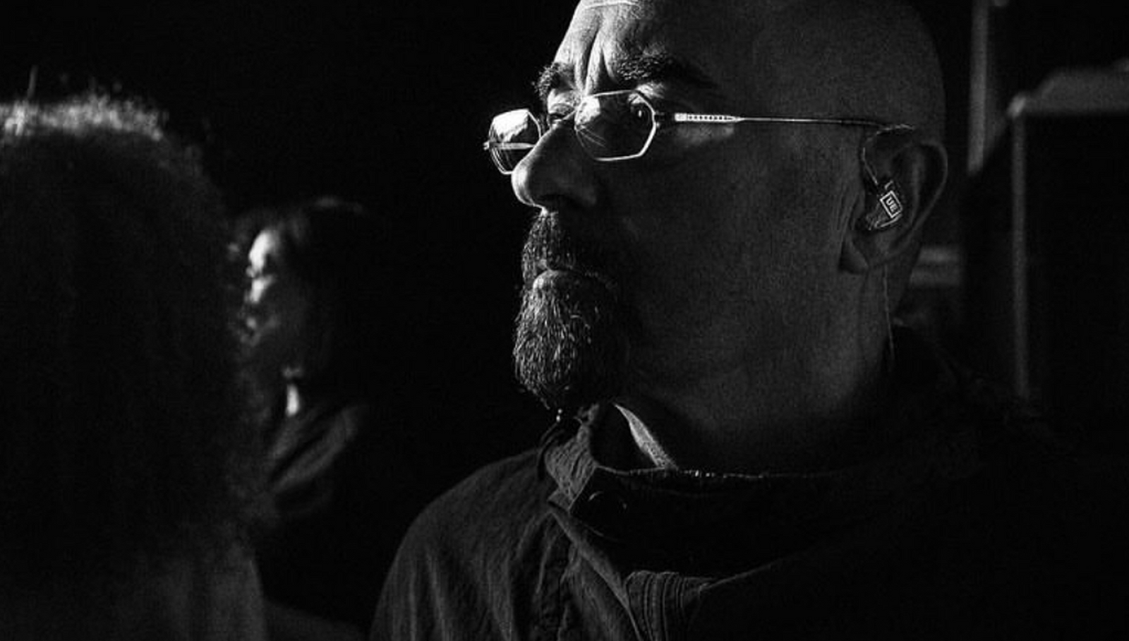 Black and white close-up of Oasis, Paul “Bonehead” Arthurs, wearing glasses with a blurred background