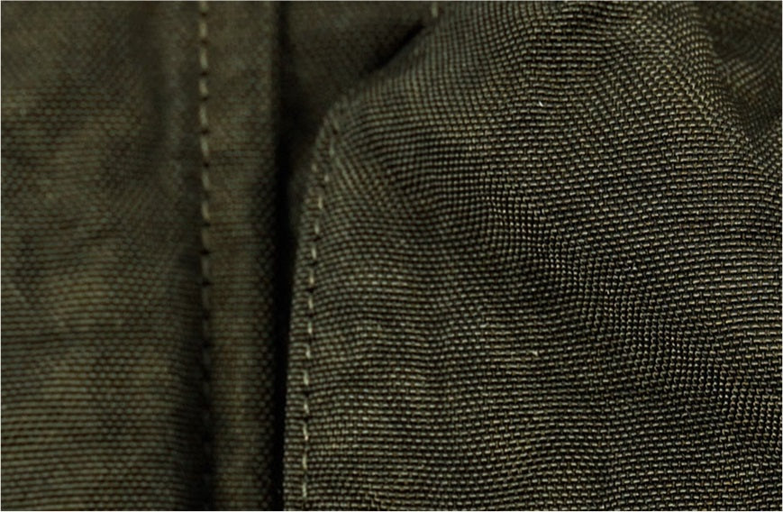Closeup of Left Hand garment dyeing: dark green textured fabric with visible stitching, showcasing unique dyed finish.